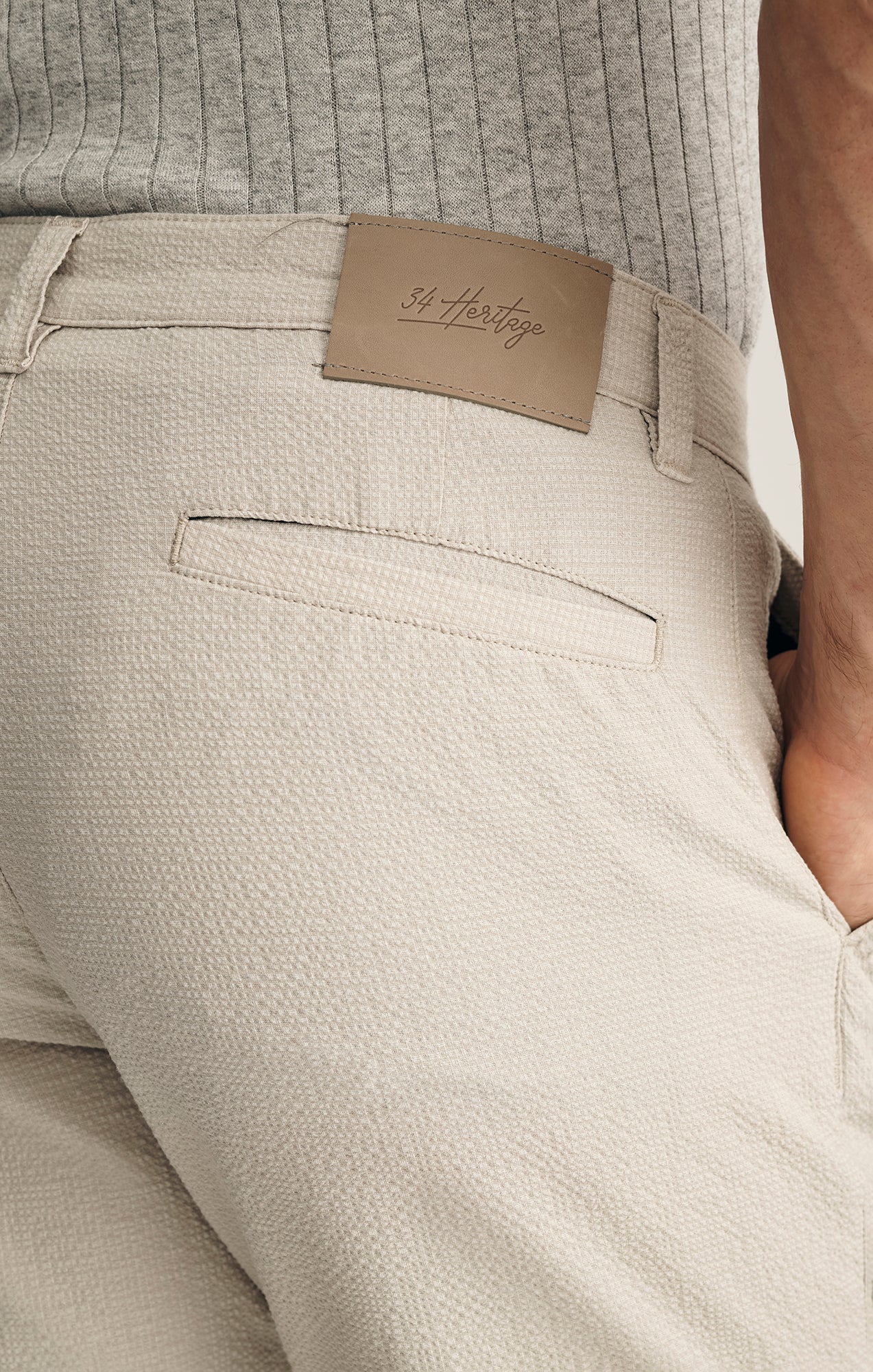 Close-up of a person wearing 34 Heritage Arizona Seersucker Shorts in light beige, made from breathable performance fabric with a leather 34 Heritage label on the waistband, paired with a grey ribbed shirt tucked in.