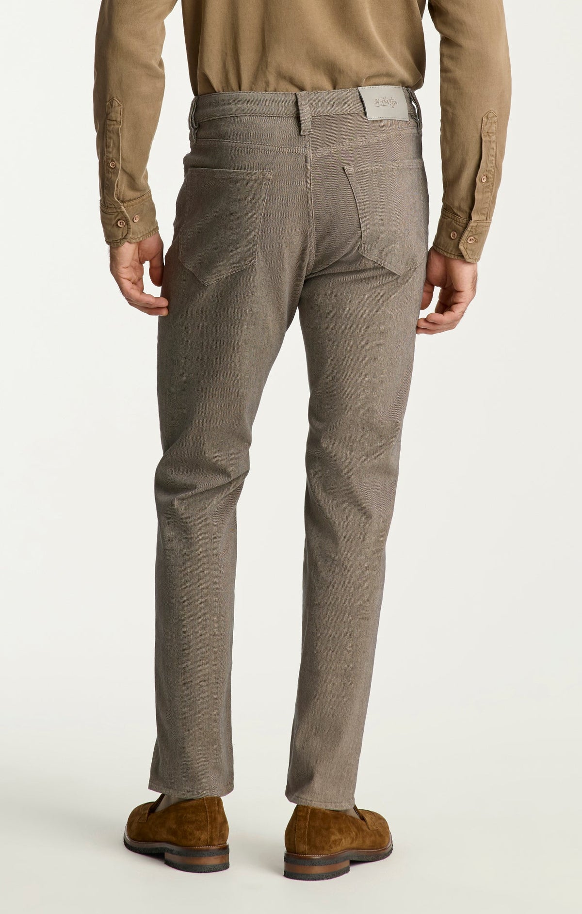 A person wearing 34 Heritage Charisma Diagonal Jeans Big & Tall, a tan shirt, brown belt, and brown suede shoes, shown from the back against a plain background.