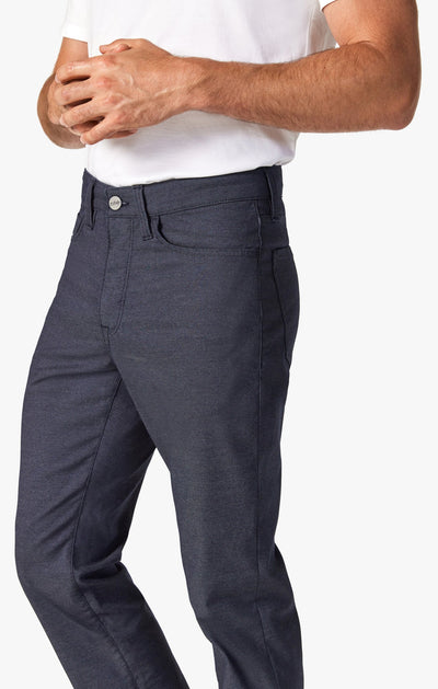 A person stands with hands clasped in front, wearing a white t-shirt and 34 Heritage Navy Coolmax temperature-regulating pants by 34 Heritage, against a plain background.