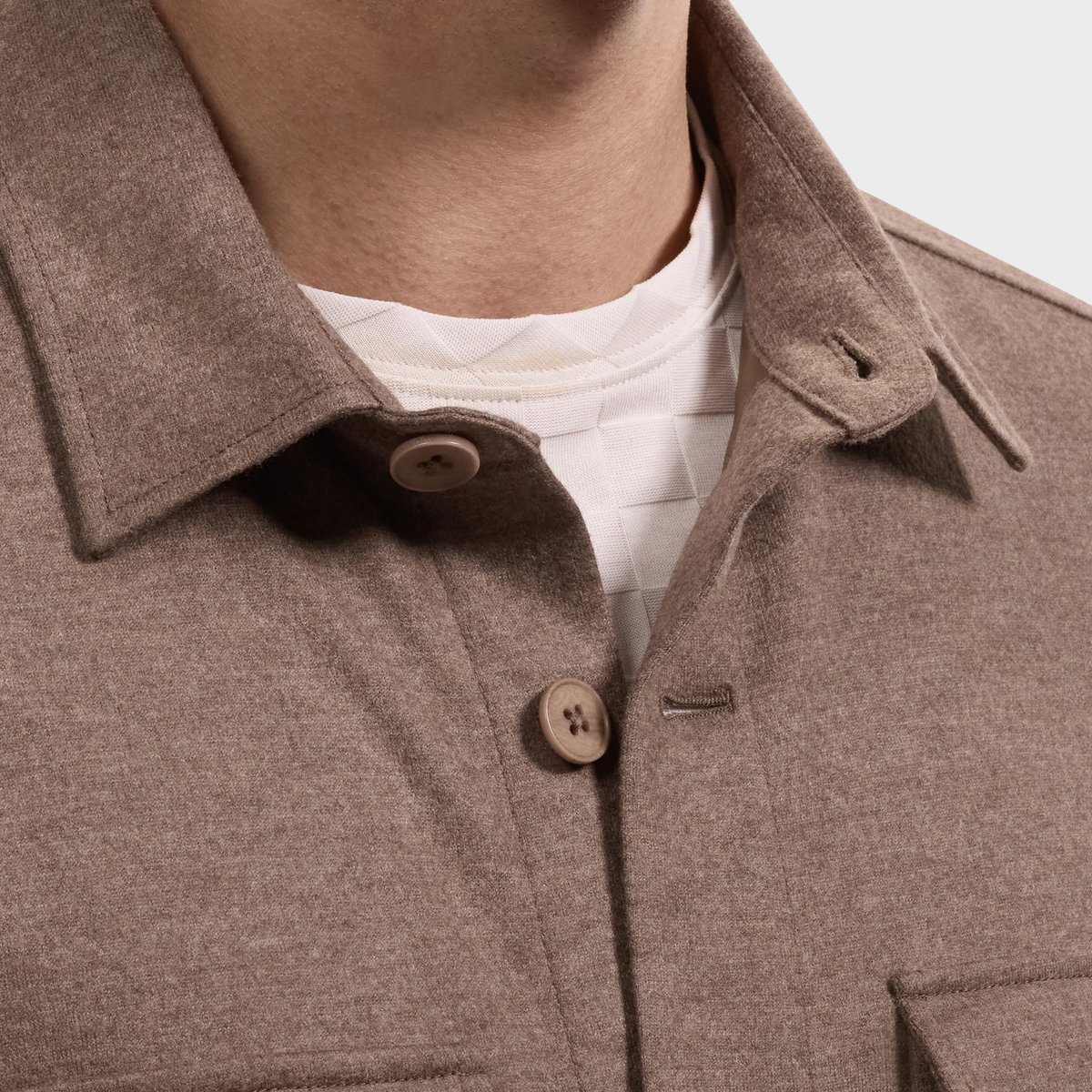 Close-up of a person wearing the Bugatchi Button Shirt Jacket KX9015JS1, featuring Bugatchi’s wrinkle-resistant fabric in brown, layered over a white textured crewneck shirt, highlighting the collar and upper chest area.