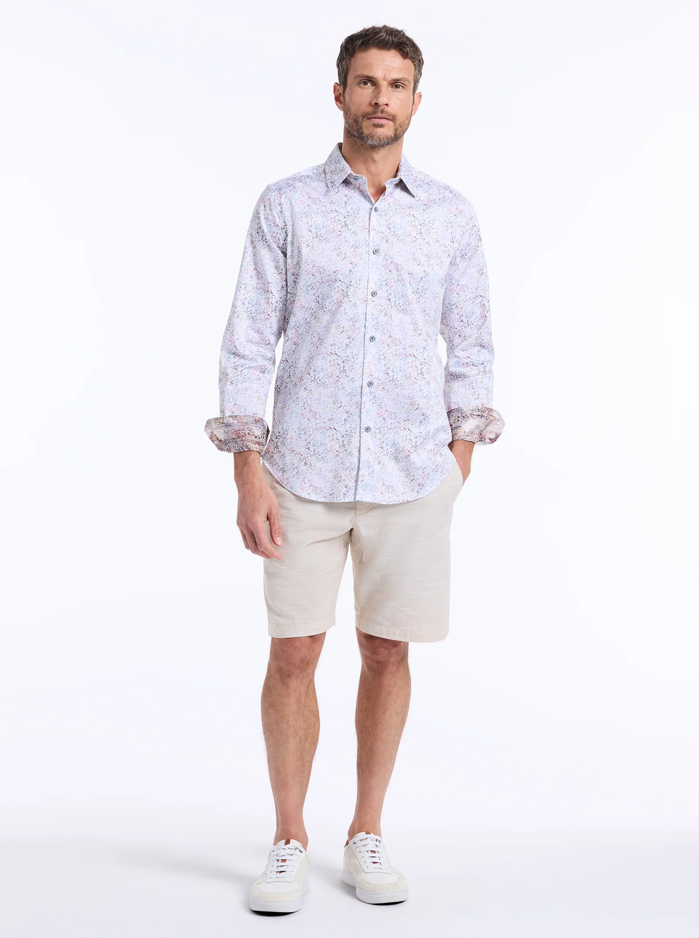 A man stands facing forward against a plain white background wearing the Robert Graham LiverPool Long Sleeve Shirt Big & Tall by Robert Graham, paired with beige shorts and white sneakers.