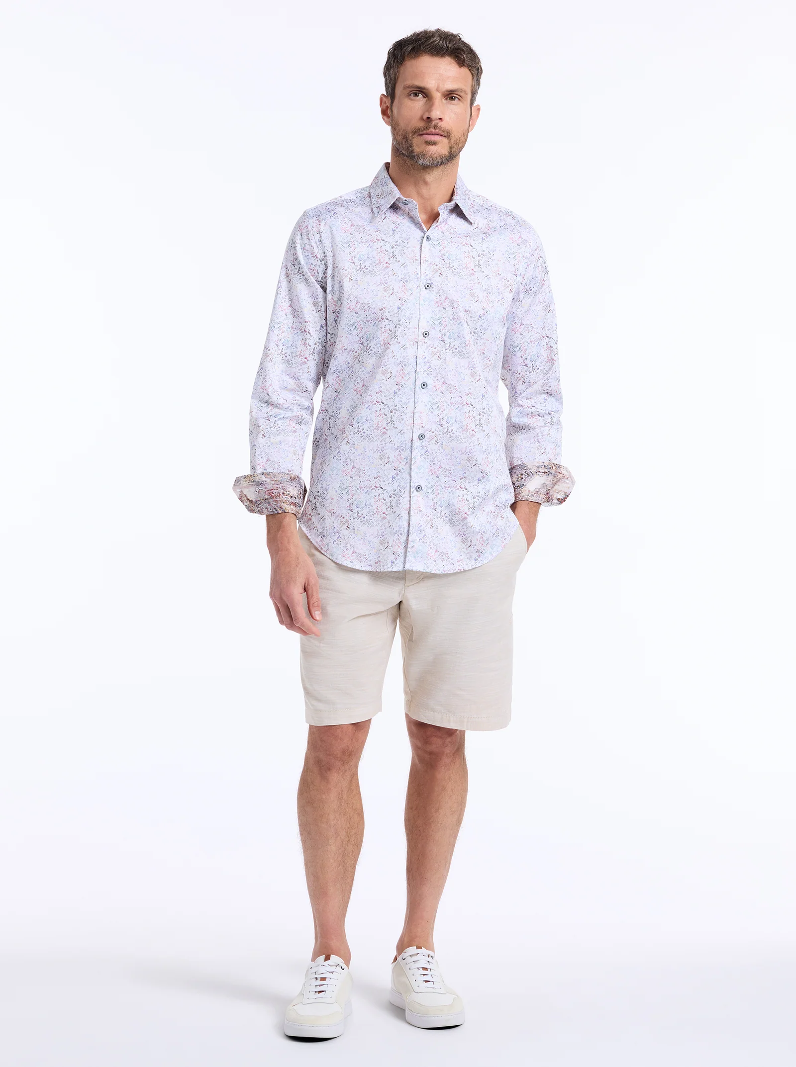 A man stands facing forward against a plain white background wearing the Robert Graham LiverPool Long Sleeve Shirt Big & Tall by Robert Graham, paired with beige shorts and white sneakers.