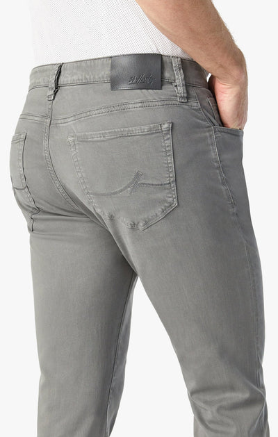 A person wears 34 Heritage Pewter Twill jeans—light gray, relaxed straight-leg style made from stretchy twill—paired with a white textured shirt, one hand in the back pocket.