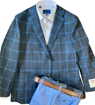 The Byron Luca Sport Coat Windowpane 9575 by Byron offers a modern fit with a blue windowpane plaid, styled over a light blue checkered shirt, complemented by light blue trousers and a brown leather belt.