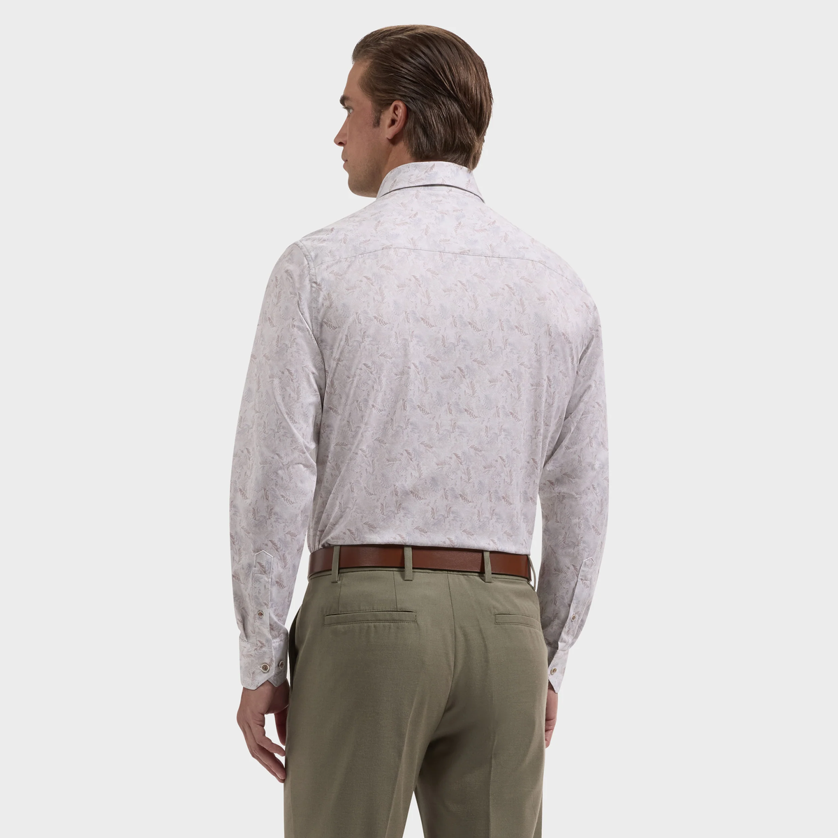 A man wearing a Bugatchi James Feather Print Sport Shirt (style KF9234K60), featuring long sleeves and a light feather pattern, along with olive green trousers, stands facing away from the camera against a plain background.