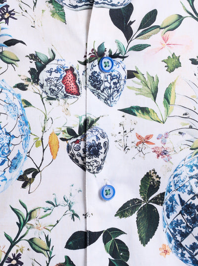 Showcasing the Robert Graham Briarcliff Woven Shirt Big & Tall, this close-up highlights a botanical print with floral and blue porcelain heart motifs accented by green leaves on a crisp white cotton-blend background. The shirt features long sleeves and two distinctive blue buttons, adding a refined touch typical of Robert Graham’s signature style.