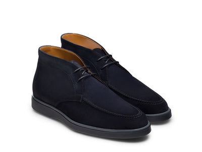 The Magnanni Lello Suede Chukka Boot by Magnanni is a pair of men’s navy suede chukka boots, inspired by classic desert boots, featuring black rubber soles and a brown inner lining, displayed on a white background.