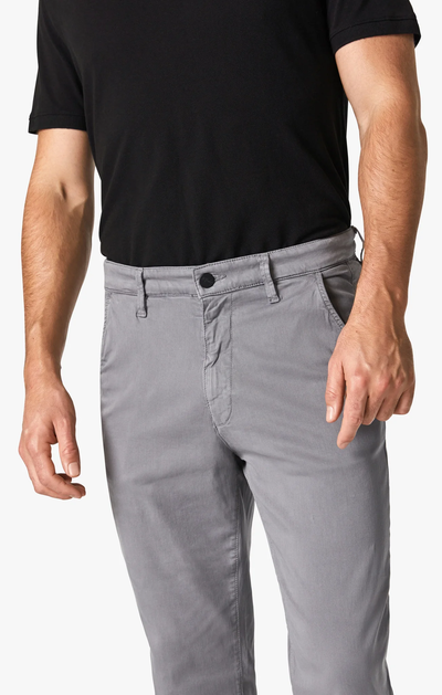 A person wearing a black short-sleeve shirt and 34 Heritage Charisma Shark Twill Big & Tall light gray straight leg chino pants, shown from shoulders to mid-thigh, with one arm relaxed at their side.
