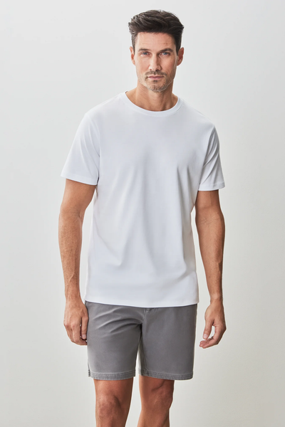 A man wears the Robert Barakett Georgia Tee Big & Tall 23336, a plain white Pima cotton crew neck T-shirt by Robert Barakett, paired with gray shorts and stands against a light-colored background.