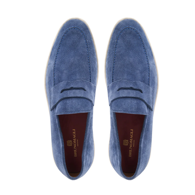 The Bruno Magli Prato Slip On Loafer is a blue suede loafer with white soles, seen from above. Its brown insoles display gold Bruno Magli branding.