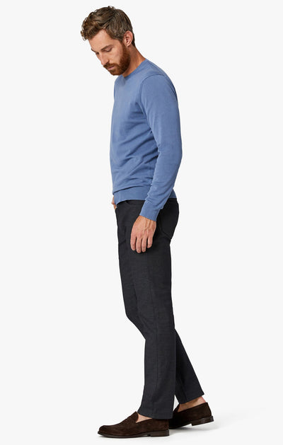 A man stands in profile wearing a blue long-sleeve shirt, 34 Heritage Black Coolmax pants by 34 Heritage, and brown loafers against a plain white background.