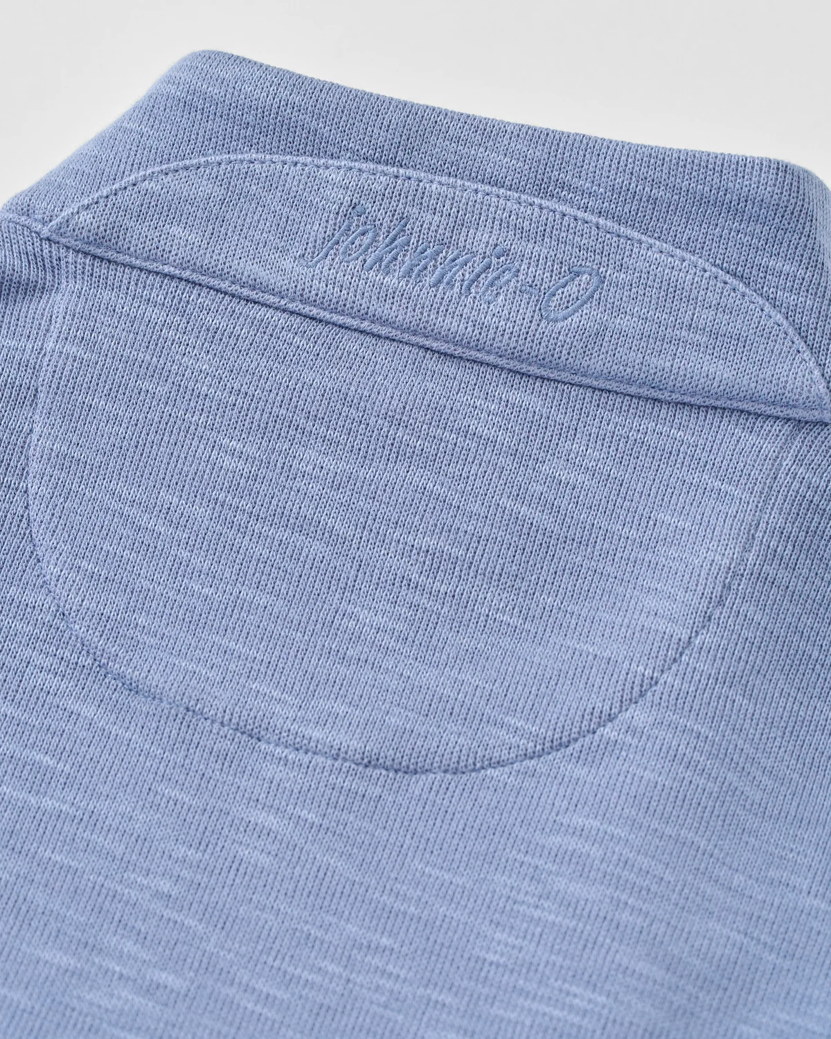 Close-up of a blue Johnnie-O Flame Stitch 1/4 Zip Sweater Big & Tall, featuring a stitched brand logo on the back neck yoke.
