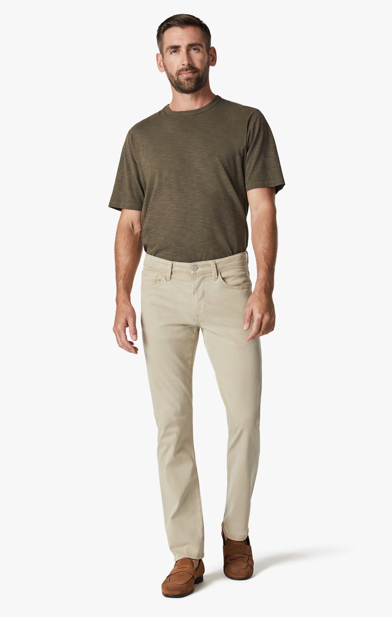 A man faces forward against a plain white background, wearing a short-sleeve olive t-shirt and 34 Heritage Aluminum Twill light beige stretchy relaxed straight-leg pants, paired with brown loafers.