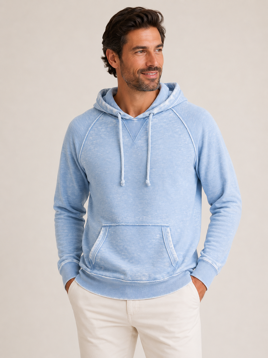 A man wearing the Georg Roth Malibu Hoodie PHW in light blue, featuring a front pocket and white drawstrings by Georg Roth, paired with off-white pants and standing against a plain background.