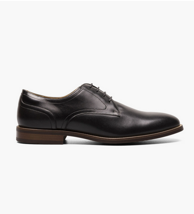 The Florsheim Rucci Plain Toe Oxford is a black leather men’s dress shoe with a brown sole, shown in profile on a white background. This versatile Florsheim shoe is perfect for formal occasions.