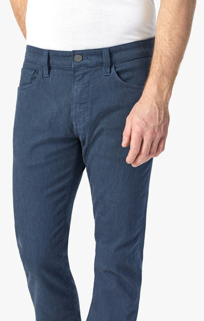 A person wears 34 Heritage Courage Diagonal Pants in a coffee hue with a straight fit and diagonal weave, paired with a white shirt, their right hand relaxed at their side.