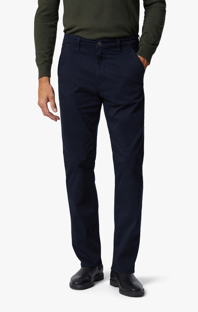 A person wearing a dark green long-sleeve shirt, 34 Heritage Charisma Navy Twill Jeans, and black shoes stands with one hand in their pocket against a white background.