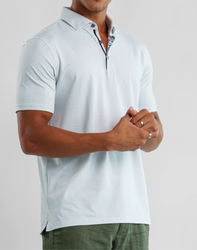 A man in a light grey Stone Rose Apex Birdseye Polo BSCSSP51 and green pants stands with hands clasped—a modern classic from Stone Rose for any summer wardrobe.