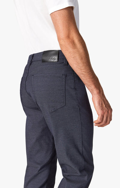 A person shown from the back and side wearing a white shirt and 34 Heritage Navy Coolmax denim pants featuring a black leather waistband patch.