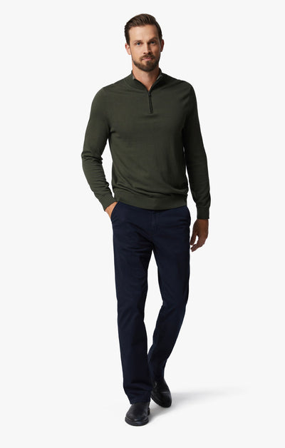 A man wearing a dark green quarter-zip sweater, 34 Heritage Navy Twill pants in a relaxed straight-leg fit, and black shoes walks forward against a plain white background.