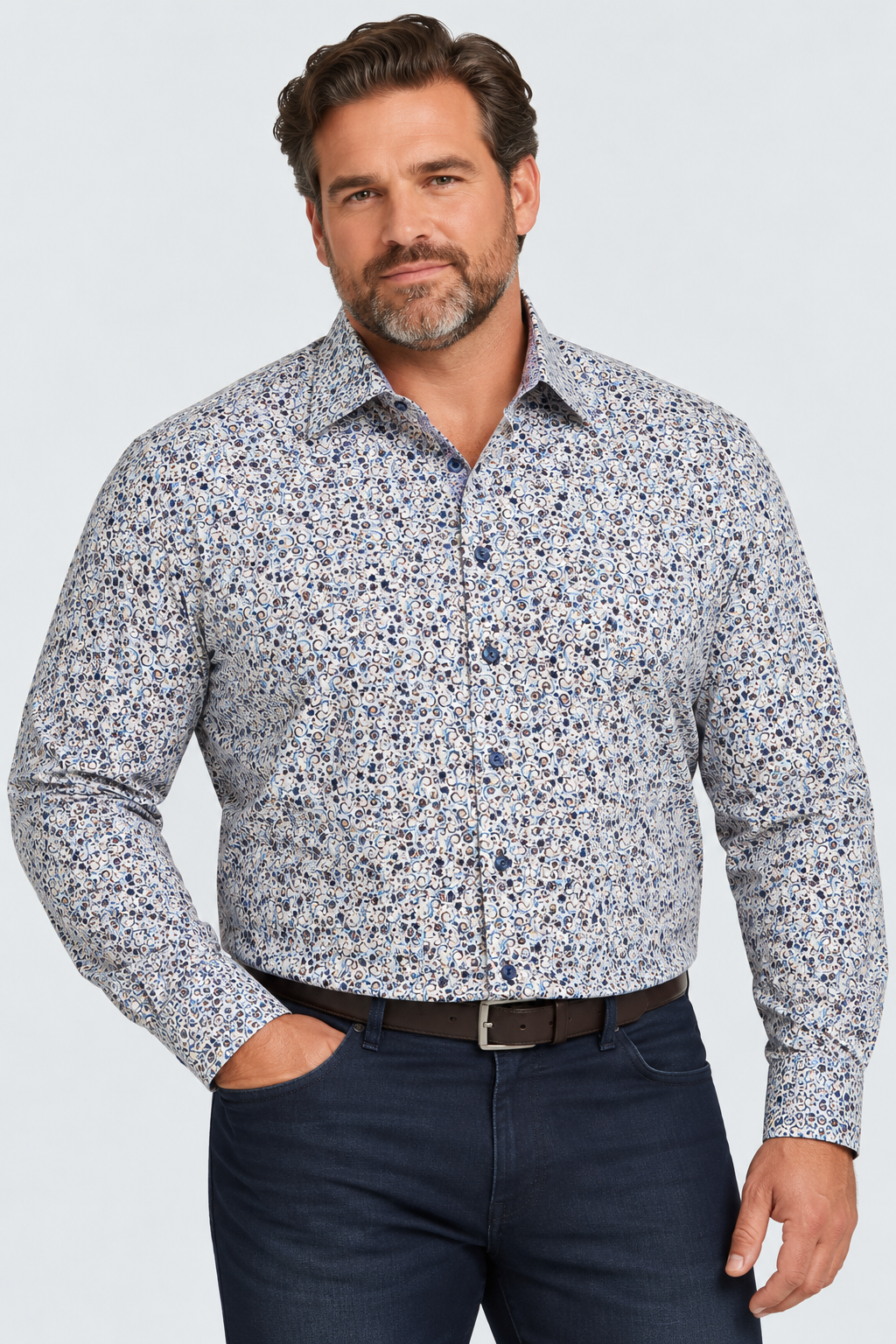A man wears a 7 Downie St. Multicolored Abstract Sport Shirt Big & Tall 26113 featuring a multicolored abstract floral print, tucked into dark denim jeans with a brown belt.