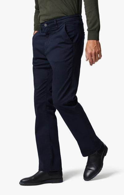 A person wearing a green long-sleeve shirt, 34 Heritage Navy Twill pants in a relaxed straight-leg fit, and black shoes stands with one hand in their pocket against a white background.