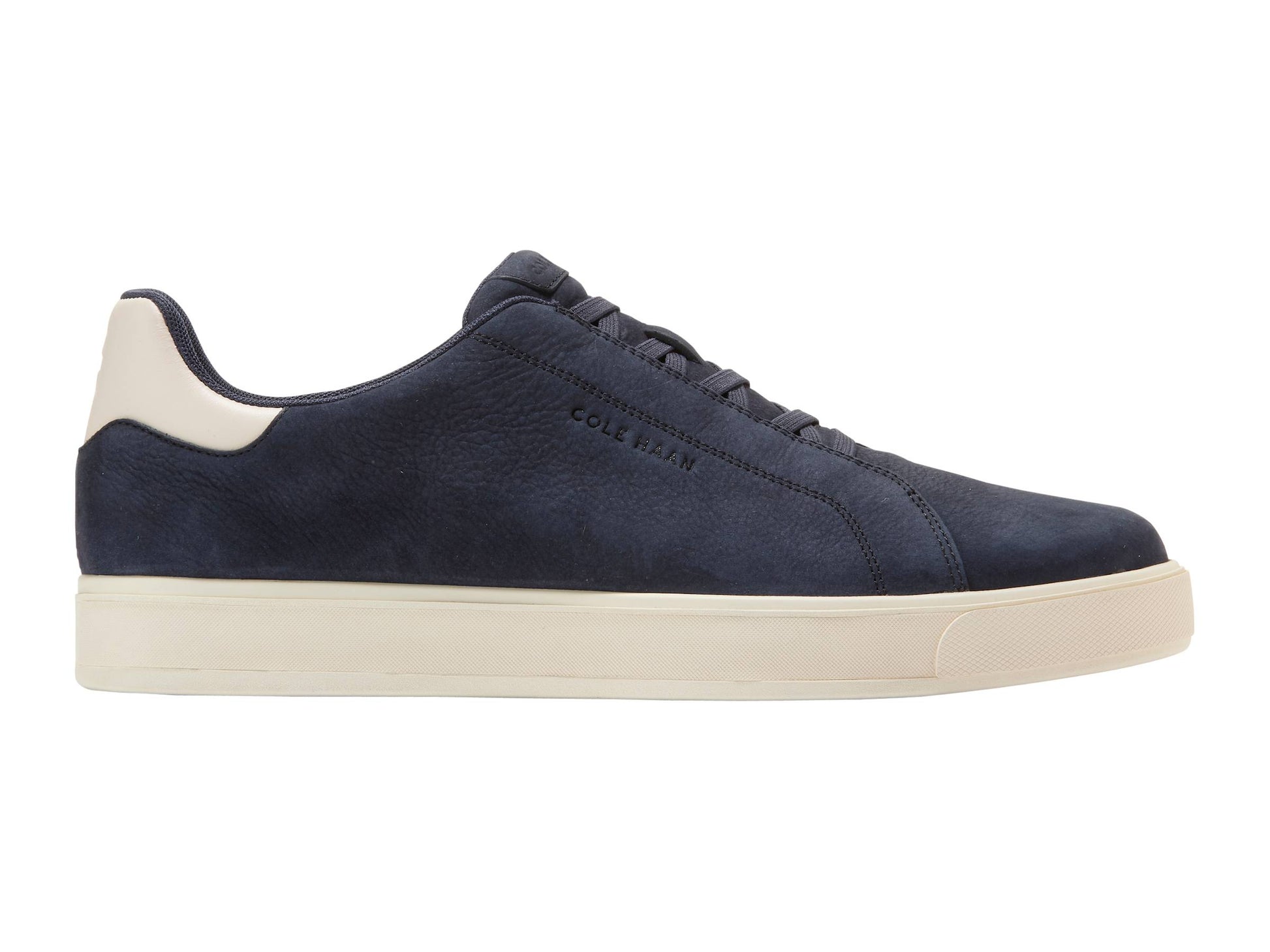 The Cole Haan GrandPro Luxe Slip On Sneaker features a navy blue suede upper, white heel tab, off-white rubber sole, and breathable design by Cole Haan, shown in a side profile view.