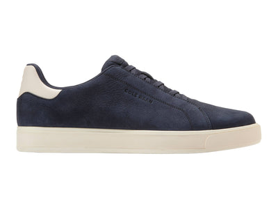 The Cole Haan GrandPro Luxe Slip On Sneaker features a navy blue suede upper, white heel tab, off-white rubber sole, and breathable design by Cole Haan, shown in a side profile view.