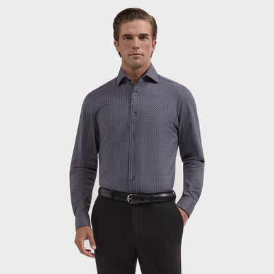 A man stands against a plain background, wearing the Bugatchi Devon Medallion Sport Shirt (KF9433K80), a dark geometric print button-up by Bugatchi, tucked into black pants with a belt.