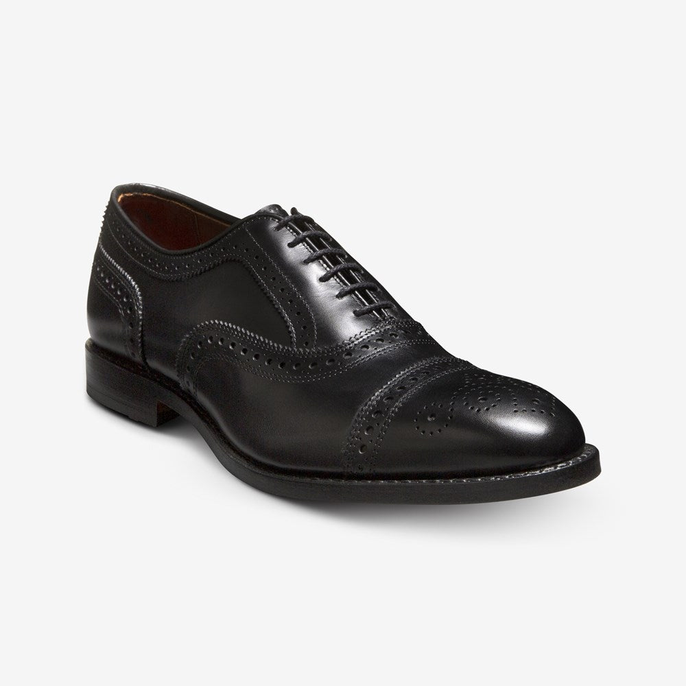 The Allen Edmonds Strand is a black calfskin oxford dress shoe from Allen Edmonds featuring brogue detailing, closed lacing, and a low heel, shown on a white background.