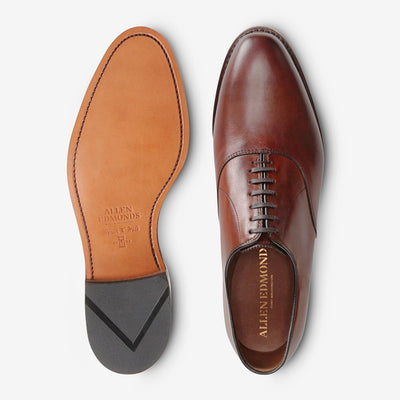 A pair of handcrafted brown Allen Edmonds Carlyle leather Oxfords—one shown from the top, the other highlighting the branded sole and signature bench welt construction.