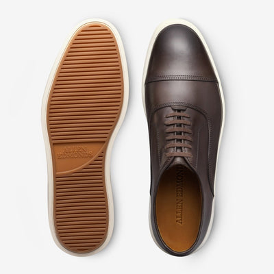 The Allen Edmonds Park Avenue Oxford Dress Sneaker features premium leather, white rubber soles with tan tread, and is shown from top and bottom views.