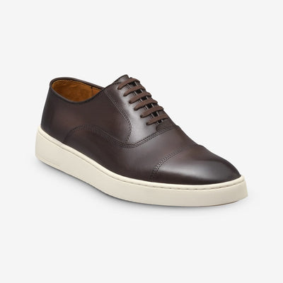 The Allen Edmonds Park Avenue Oxford Dress Sneaker by Allen Edmonds features brown premium leather and a white rubber sole, displayed at a three-quarter angle against a plain white background.