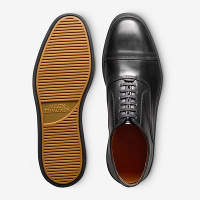 A pair of Allen Edmonds Park Avenue Oxford Dress Sneakers: one displays the classic black leather lace-up top, the other reveals a tan rubber sole with the Allen Edmonds logo.