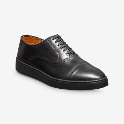 The Allen Edmonds Park Avenue Oxford Dress Sneaker by Allen Edmonds features premium black leather, a cap toe, black laces, and a black rubber sole, shown on a white background.