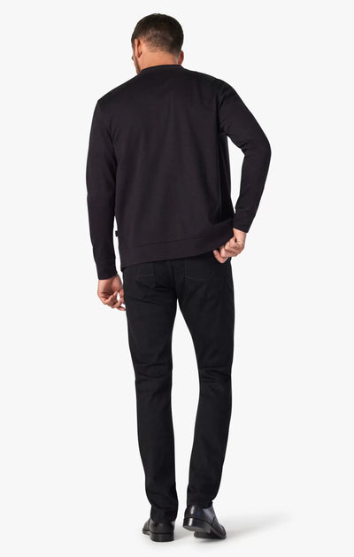 A man stands facing away, wearing a black long-sleeve shirt, black shoes, and 34 Heritage Courage Black Urban Jeans by 34 Heritage against a plain white background.