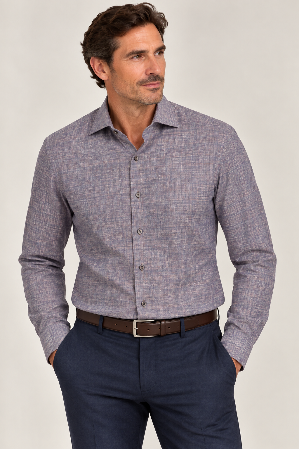 A man wearing the Elite Serica Elite Textured Print Sport Shirt (EX2674150), expertly tailored in a light purple patterned fabric and tucked into dark blue pants with a brown belt, stands with hands in pockets against a neutral background.