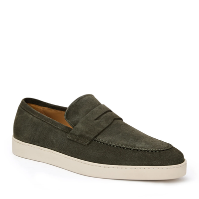 The Bruno Magli Prato Slip On Loafer in olive green suede features a white rubber sole, penny strap detail, and visible stitching. Displayed here as a single shoe against a plain white background.