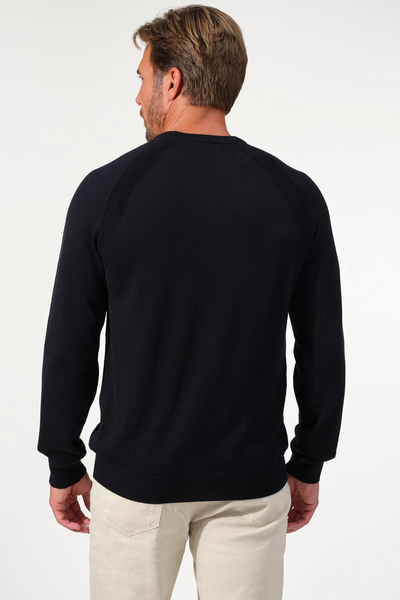 A man with light brown hair wears the black Garnet Milano Crew Sweater 2522003CS and cream pants, standing with his back to the camera against a plain white background.