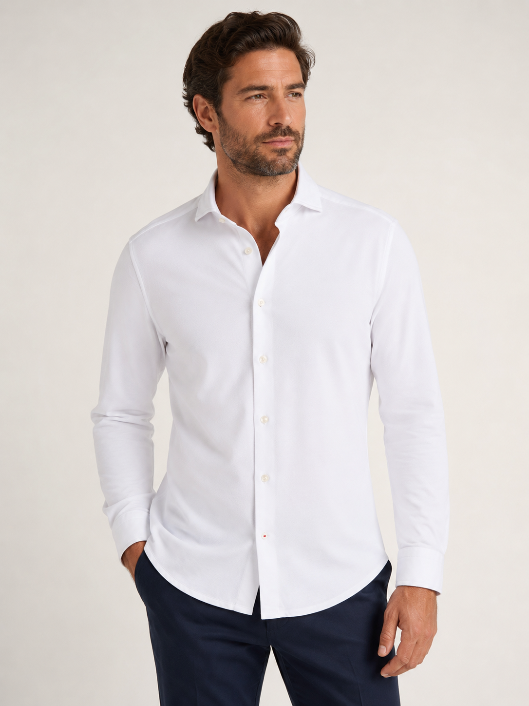 A man stands against a plain background wearing the Stone Rose ORIGIN - Long Sleeve T-Series Sport Shirt paired with dark trousers, looking to his right with one hand in his pocket.