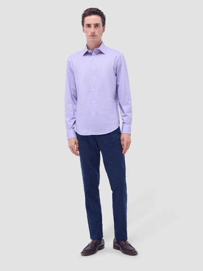 A man stands against a light grey background wearing the Bugatchi James Sport Shirt in Lilac by Bugatchi, paired with navy blue pants and dark brown shoes.