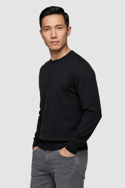 A man wearing the Garnet Upton Merino Ribbed Crewneck Sweater (style 2622002) by Garnet and gray jeans stands against a plain light gray background with his left hand in his pocket, looking straight at the camera.