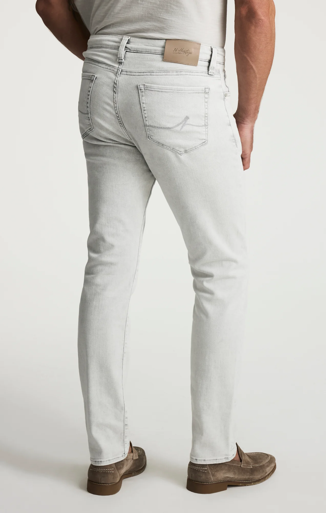 A person is shown from the back, standing against a plain white background, wearing 34 Heritage Courage Jeans Organic Ultra in light gray and brown loafers.
