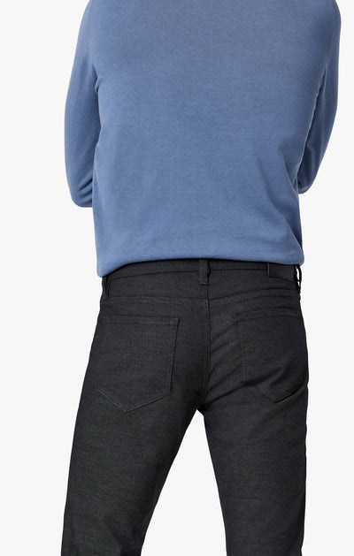 A person is shown from the back, arms crossed behind them, wearing a blue long-sleeve shirt and 34 Heritage Black Coolmax jeans by 34 Heritage against a plain white background.