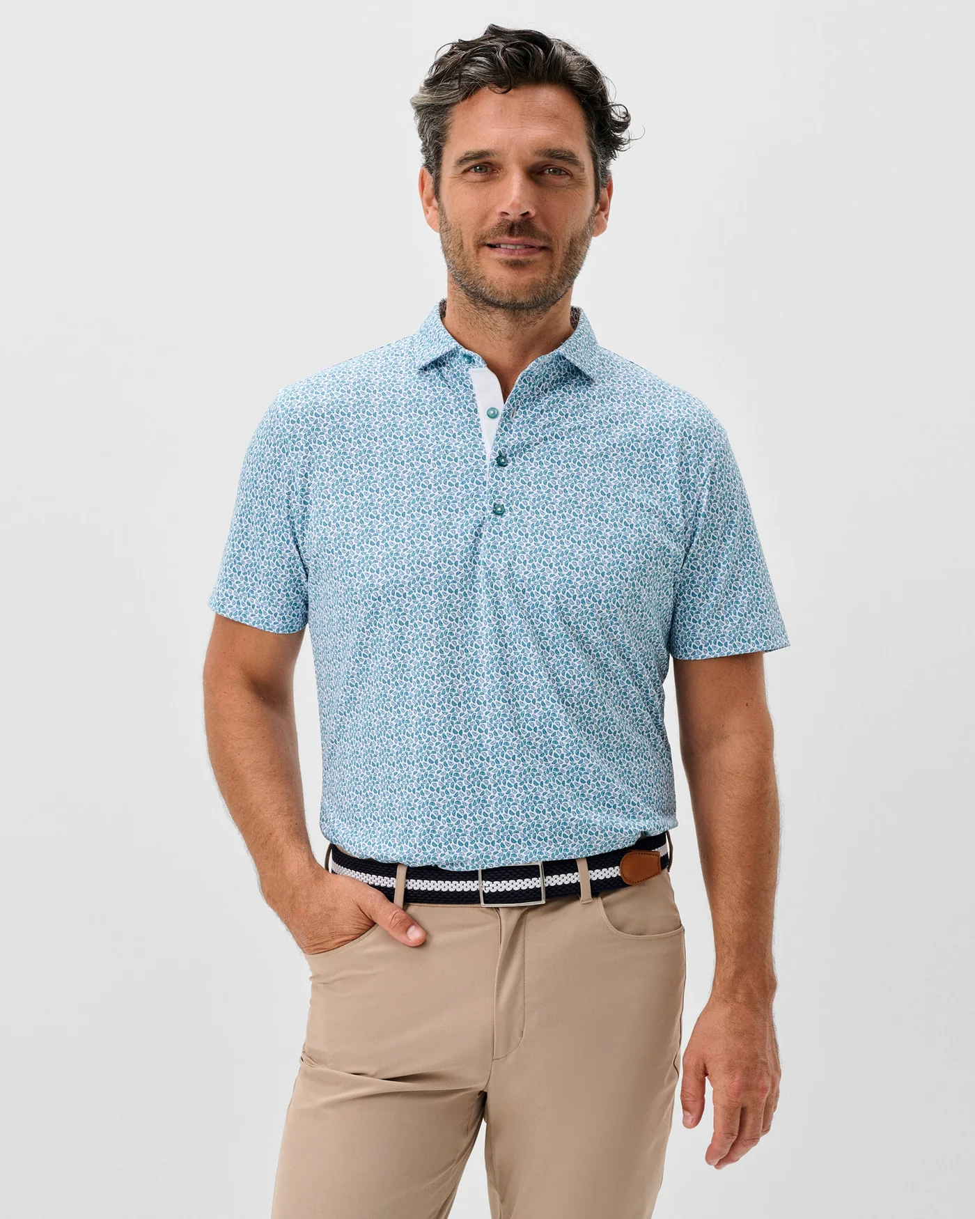 Man wearing a Johnnie-O Peelin Good Big & Tall Knit Polo short sleeve shirt, beige pants, and a black and white belt stands against a plain white background.