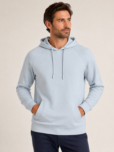 A man wearing the Georg Roth Scuba Hoodie SPH in light blue with front pockets, paired with navy pants, stands against a plain beige background.