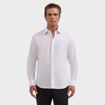 A man stands facing forward against a plain light background, wearing the Bugatchi Julian Tonal Geometric Jacquard Shirt KS4001L3S in white with long sleeves and black pants.