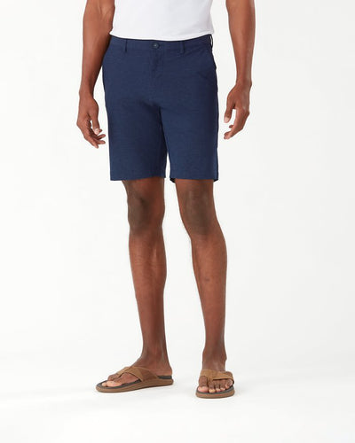 A person wearing a white shirt, Tommy Bahama Chip Shot Shorts Big & Tall in navy by Tommy Bahama, and brown sandals stands against a plain white background.