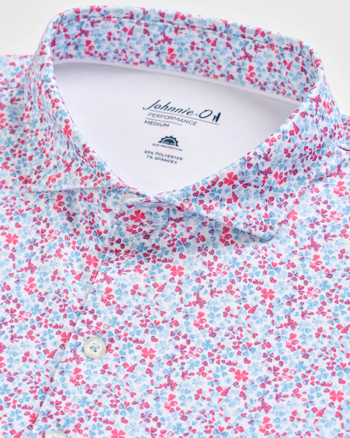 Close-up of the Johnnie-O Charmer Jersey Polo, featuring a pink and blue floral pattern and a Johnnie-O Performance label inside the collar—designed for comfort and style.