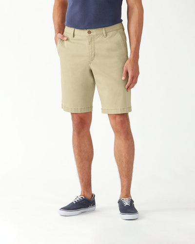 A man wearing Tommy Bahama Boracay Shorts Big & Tall in beige, a navy t-shirt, and navy sneakers stands with hands in pockets against a plain white background.
